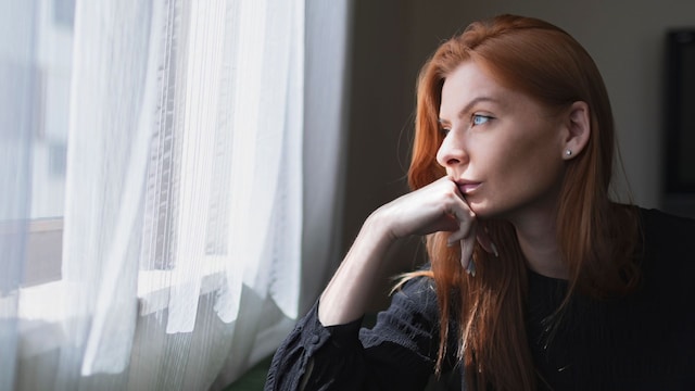 Retrato de una mujer mirando por la ventana en actitud triste
