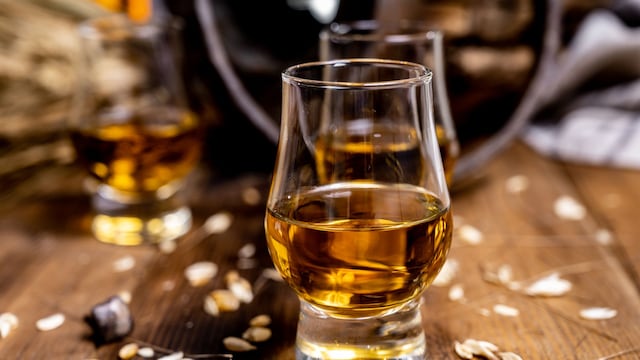 Vasos de cata para whisky con granos de cebada alrededor y barricas detrás