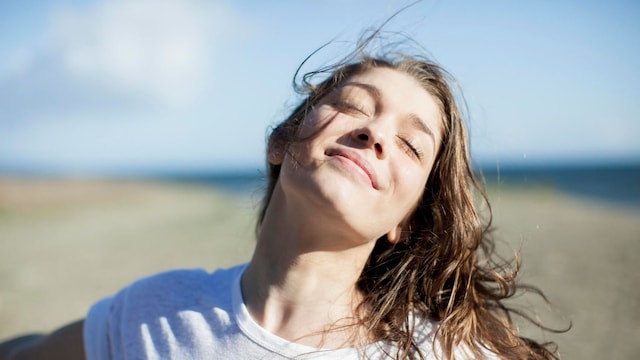 young woman with eyes closed smiling on a beach
