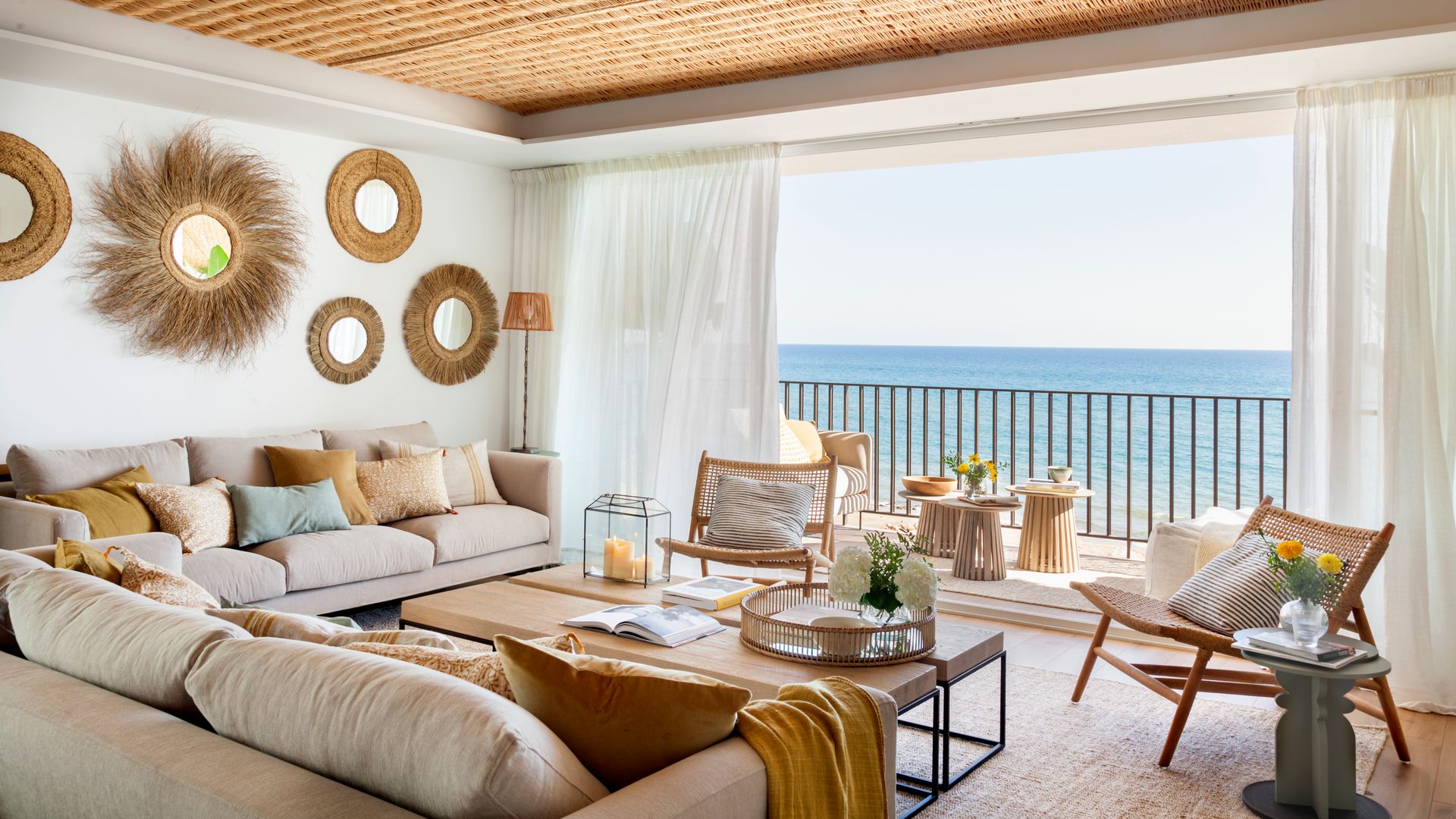 Salón casa de playa con salida a la terraza y vistas al mar, techo de rafia, sofás beiges, espejos de rafia redondos