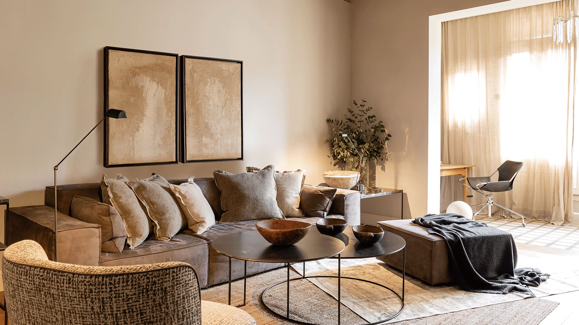 Salón con galeria con despacho, vigas de madera en el techo, sofá gris, alfombras, lámpara de pie y de sobremesa, puf, mesa de centro negra