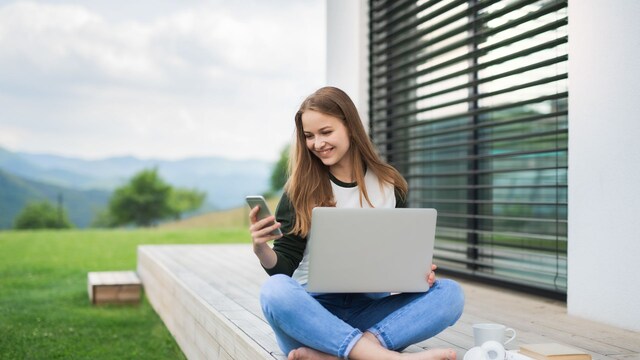 Una chica usando su teléfono y su portátil en el campo