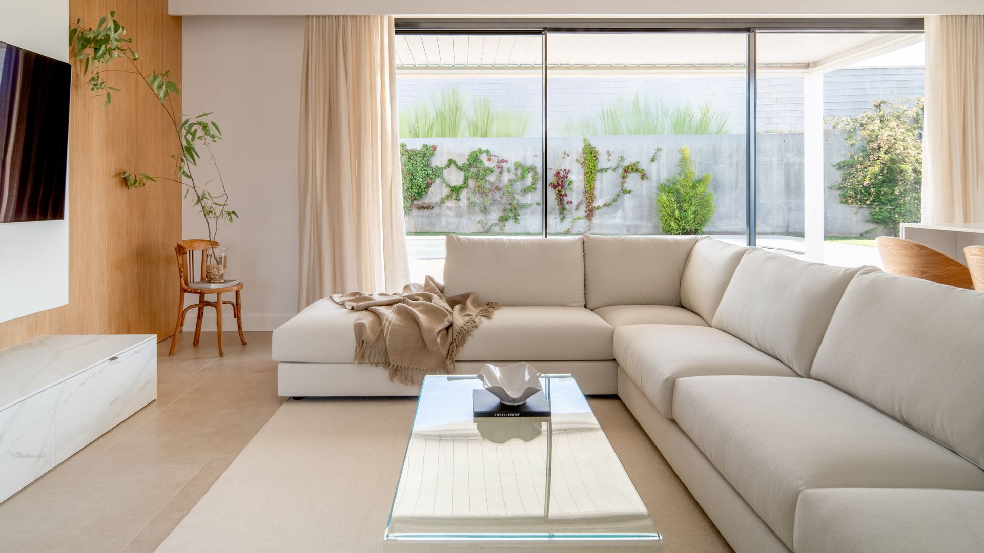 Salón minimalista con sofá blanco, ventanales con salida al jardín, mueble colgada en la pared, alfombra blanca, mesa de centro