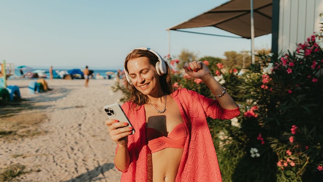 Una chica en la playa con unos auriculares y un móvil