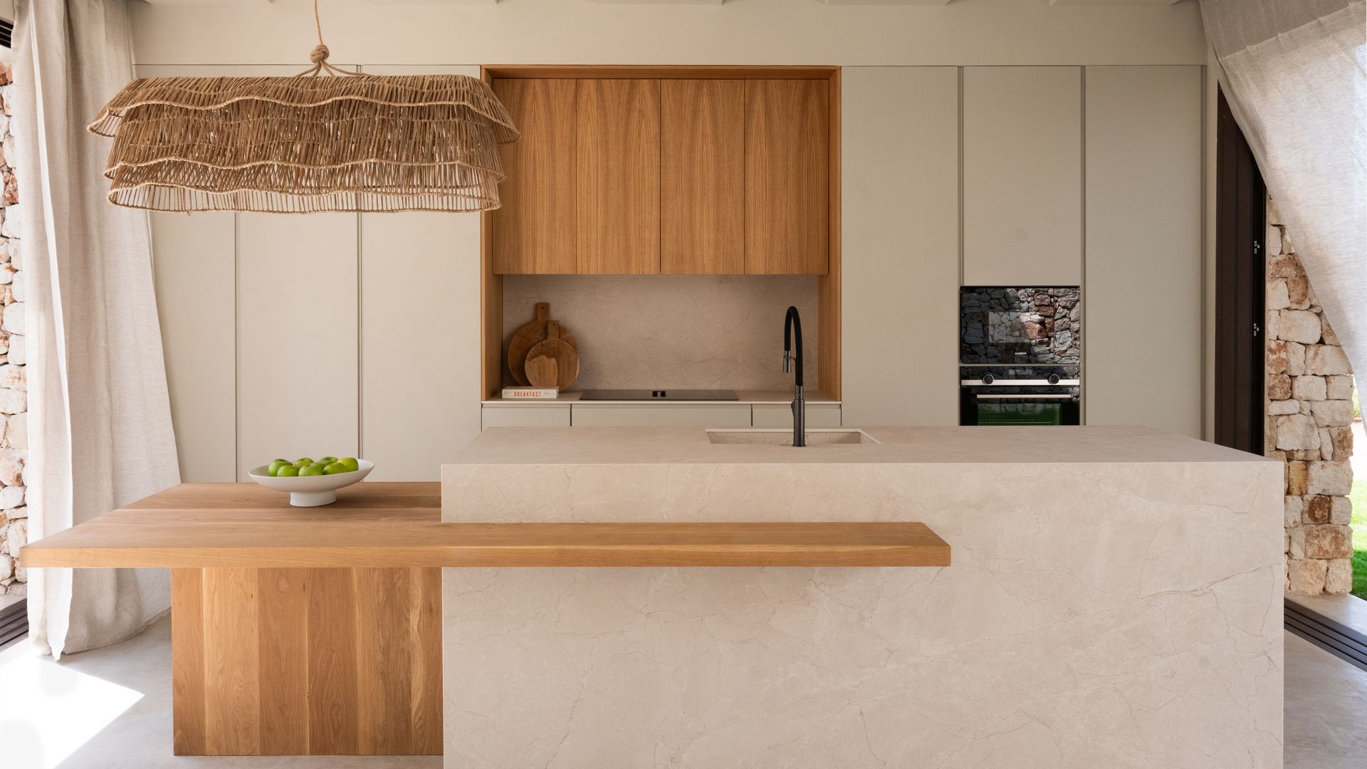 Cocina beige con isla con mesa de madera, lámpara de fibras vegetales, campana de madera, armarios sin tiradores 