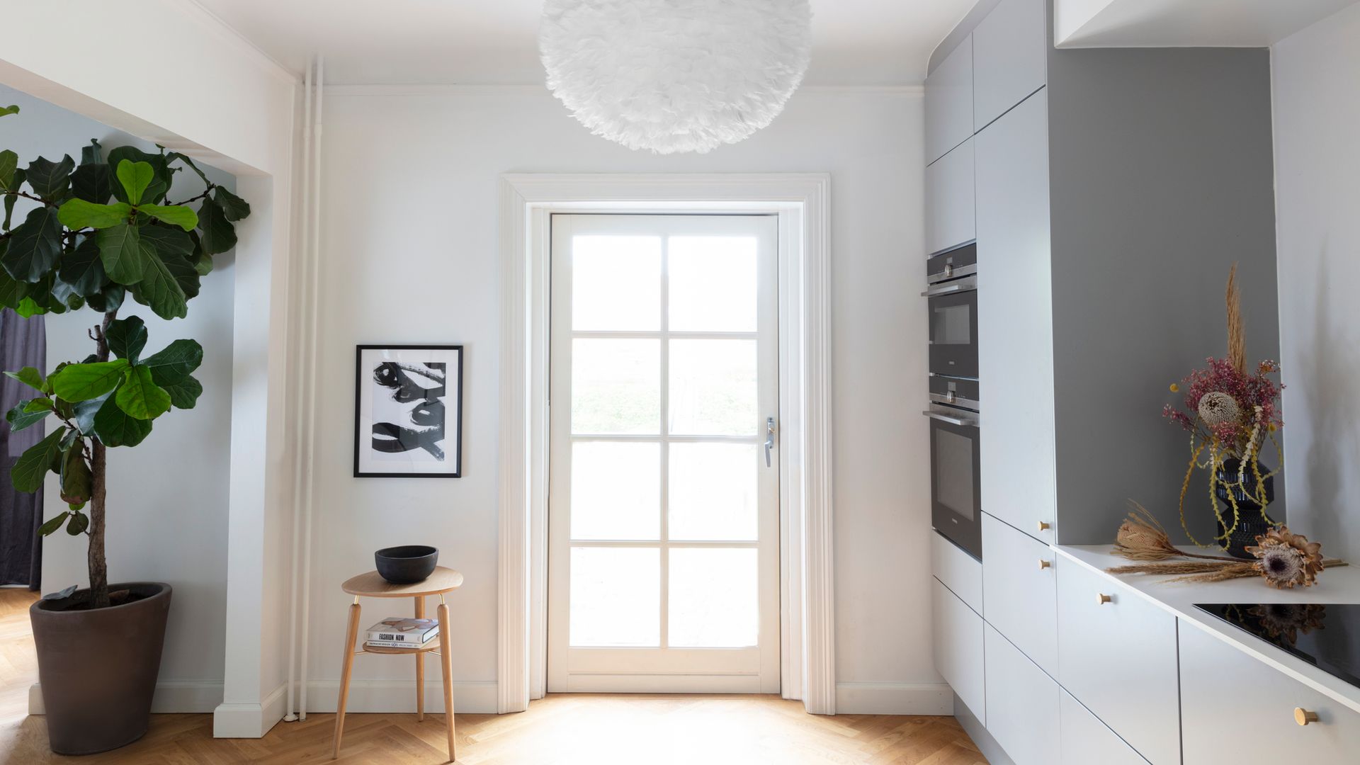 Cocina gris, con lámpara de techo de plumas, suelo de madera, taburete de madera y cuadro en la pared