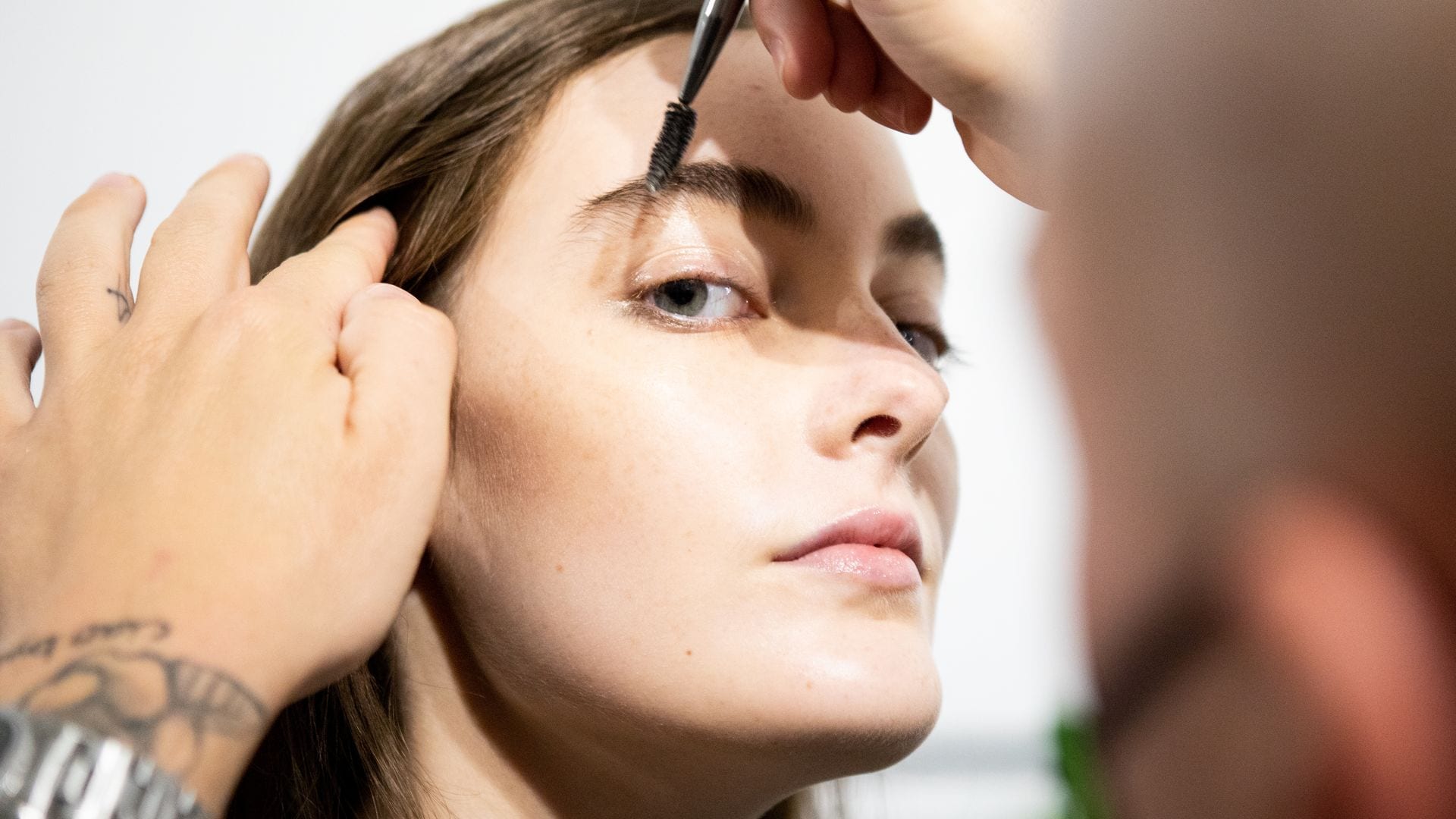 Maquillador peinando las cejas de una modelo en la Milan Fashion Week Spring/Summer 2021