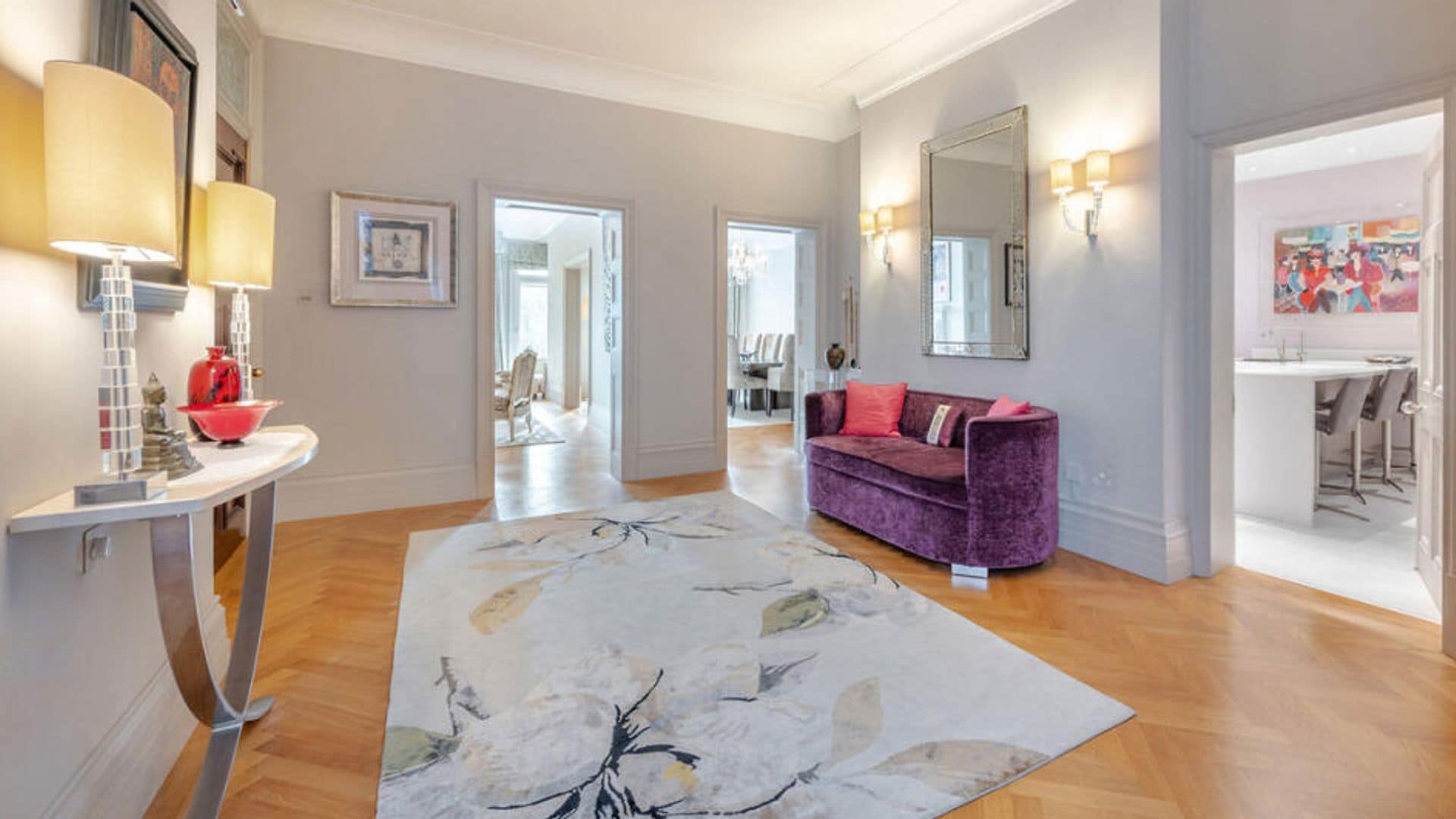 Recibidor con alfombra con sofá de terciopelo morado, consola, lámparas de sobremesa, espejo y entrada a la cocina, el salón y el comedor
