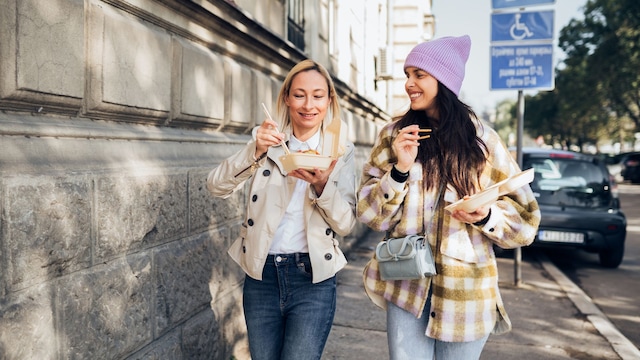 dos mujeres comiendo comida rápida mientras caminan por la calle