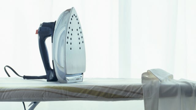 Plancha de metal sobre tabla de plancha con camisa blanca