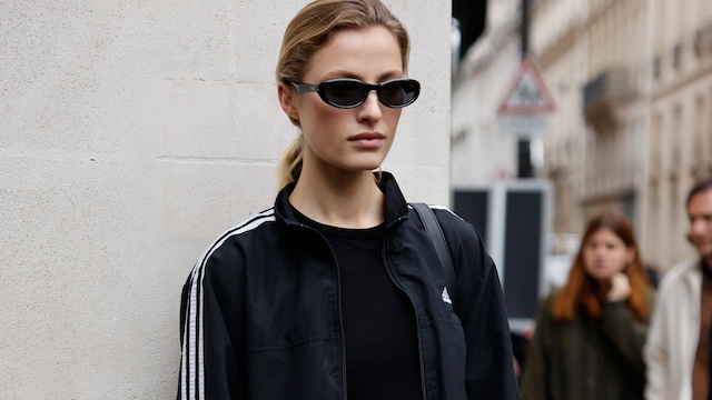 Mujer rubia con falda blanca, camiseta negra y chaqueta de Adidas en París