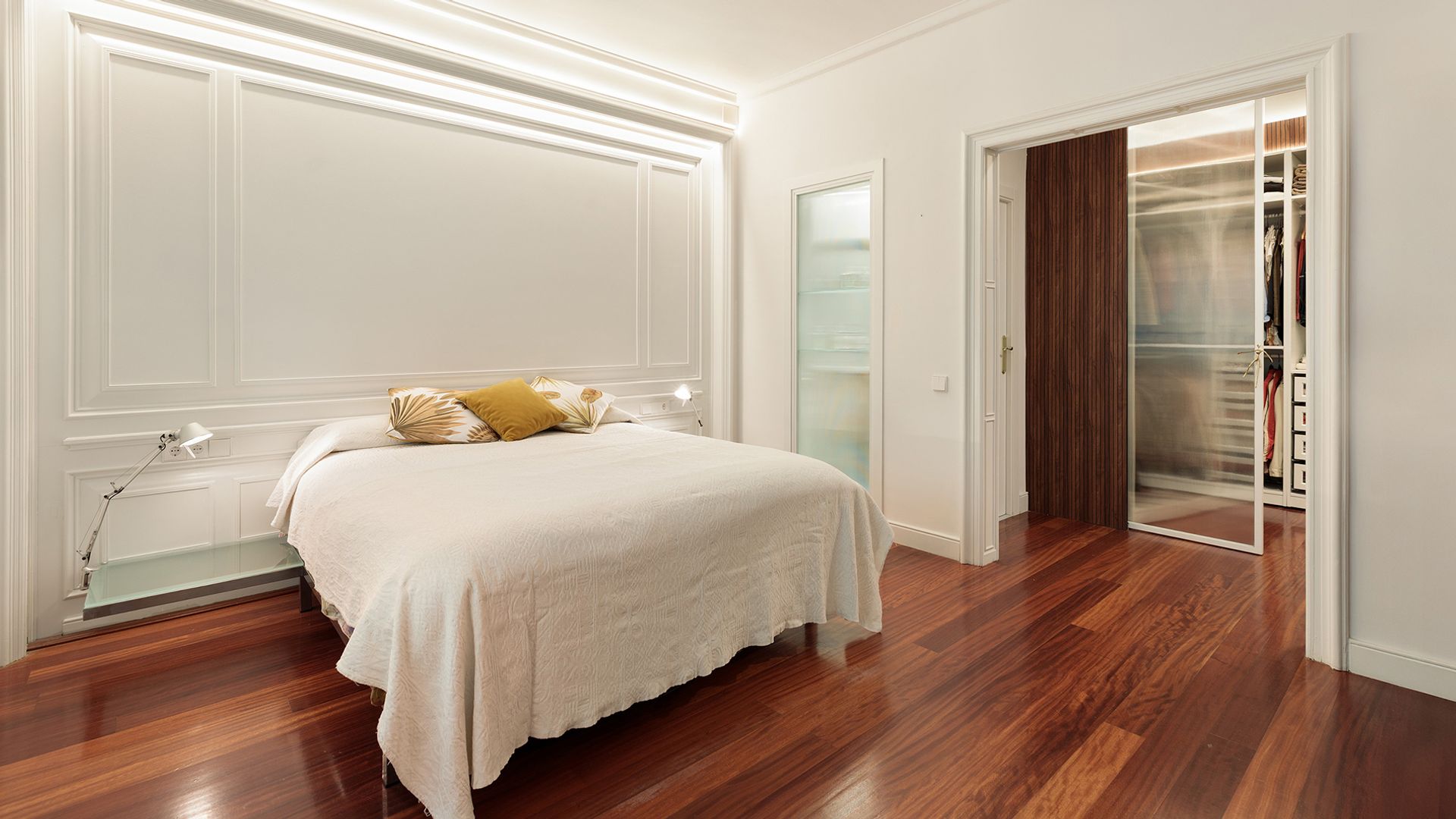 Dormitorio con panel en la pared del cabecero, suelo de madera oscura, vestidor integrado con puerta de cristal 