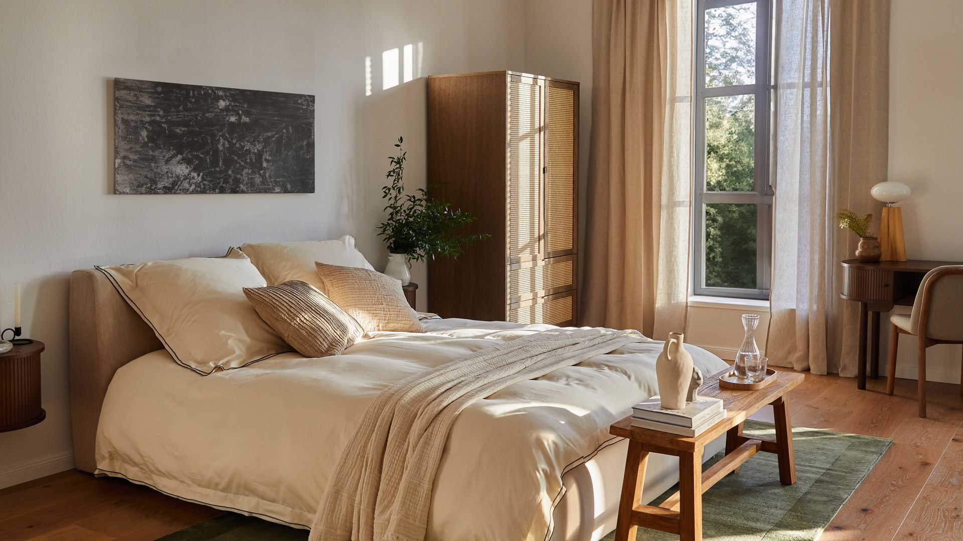Dormitorio con ropa de cama beige, cabecero tapizado, alfombra verde, suelo de madera, armario de rejilla