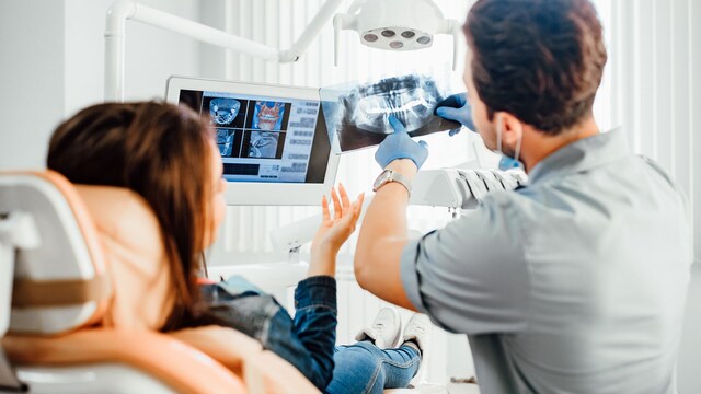 Concepto de medicina, odontología y atención médica, dentista masculino que muestra una radiografía de los dientes a una paciente en el consultorio de la clínica dental.