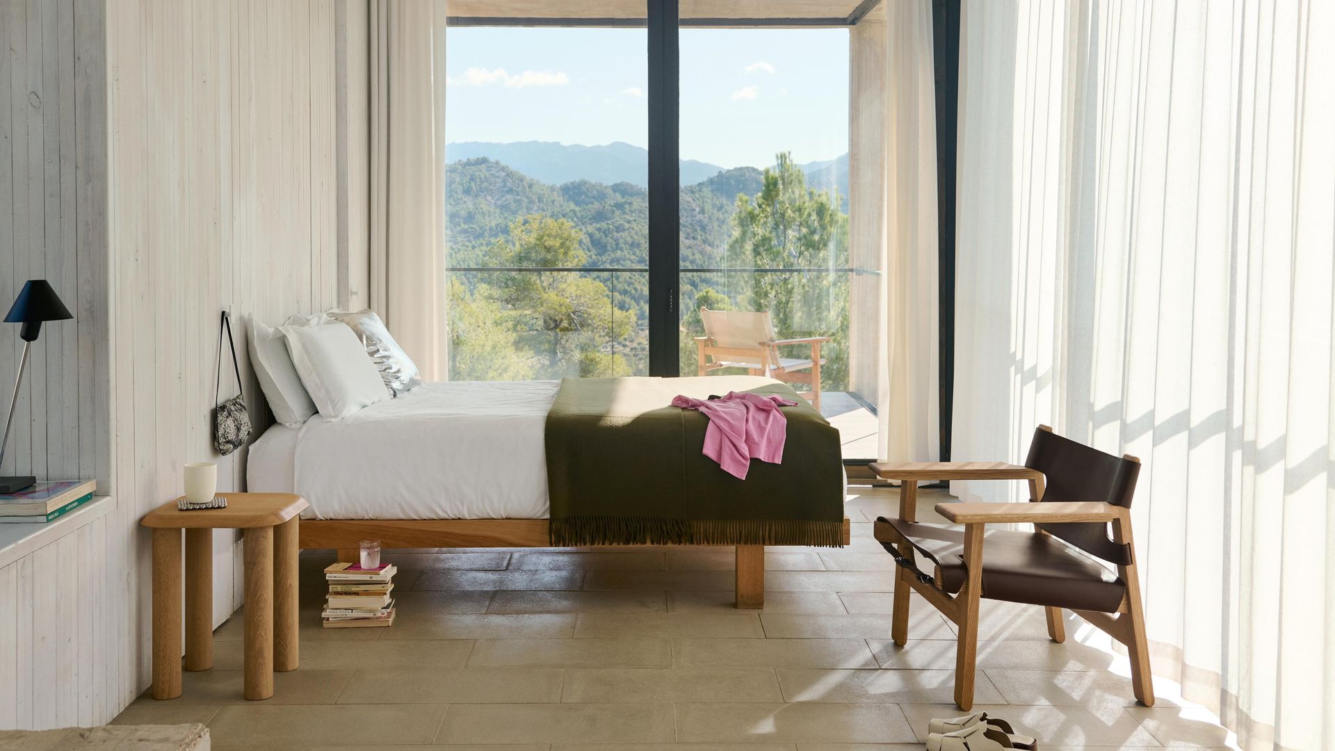 Dormitorio con salida a una terraza, silla de madera y cuero, mesita de noche, cortinas blancas, colcha verde