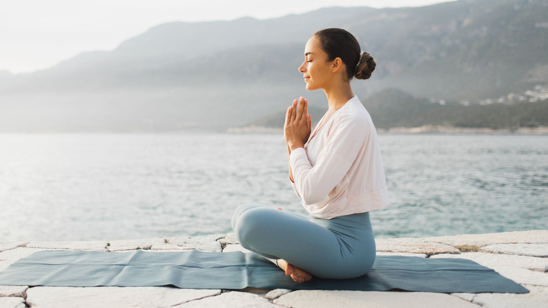 Mujer joven practicando yoga en una esterilla junto al mar