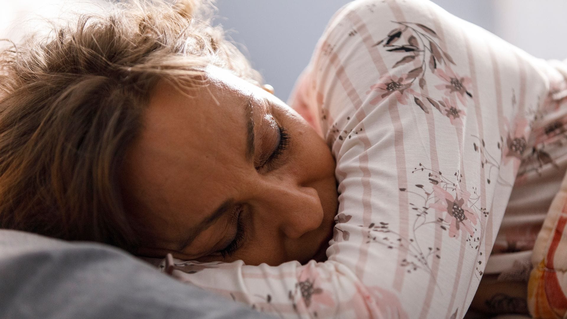 Mujer de 50 años durmiendo en la cama, con un pijama de flores, sobre la almohada. Un plano detalle de su cara.