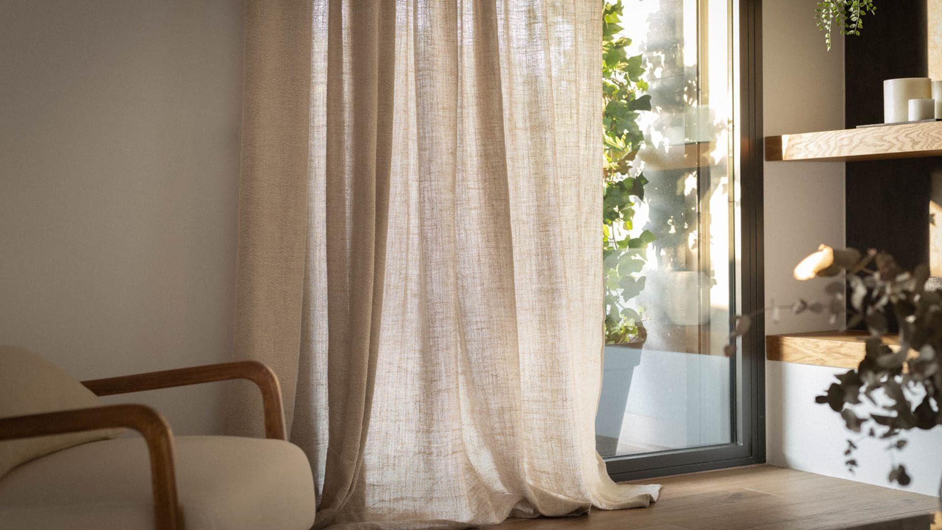 Salón con estantería de obra con baldas de madera, cortinas beiges, butaca tapizada y ventana