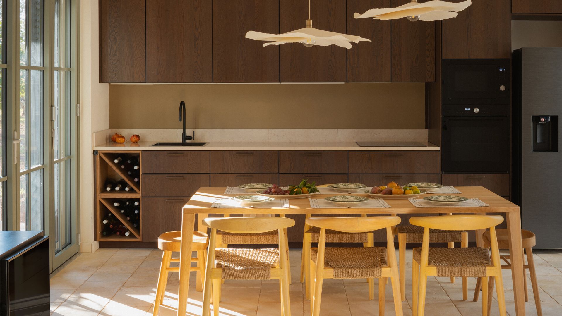 Cocina de madera oscura, con comedor, con mesa y sillas de comedor de madera clara, lámparas de techo. vinoteca