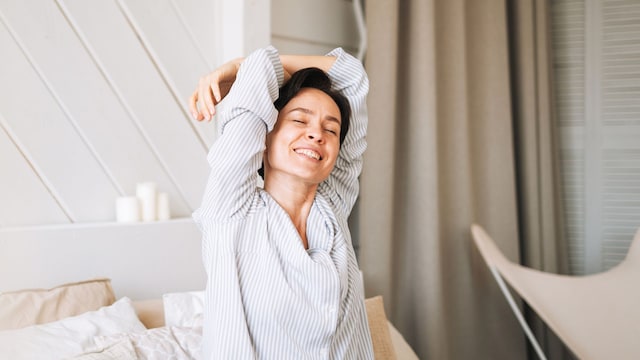 Mujer joven sonriendo en la cama al estar descansada, estirando en la cama por la mañana