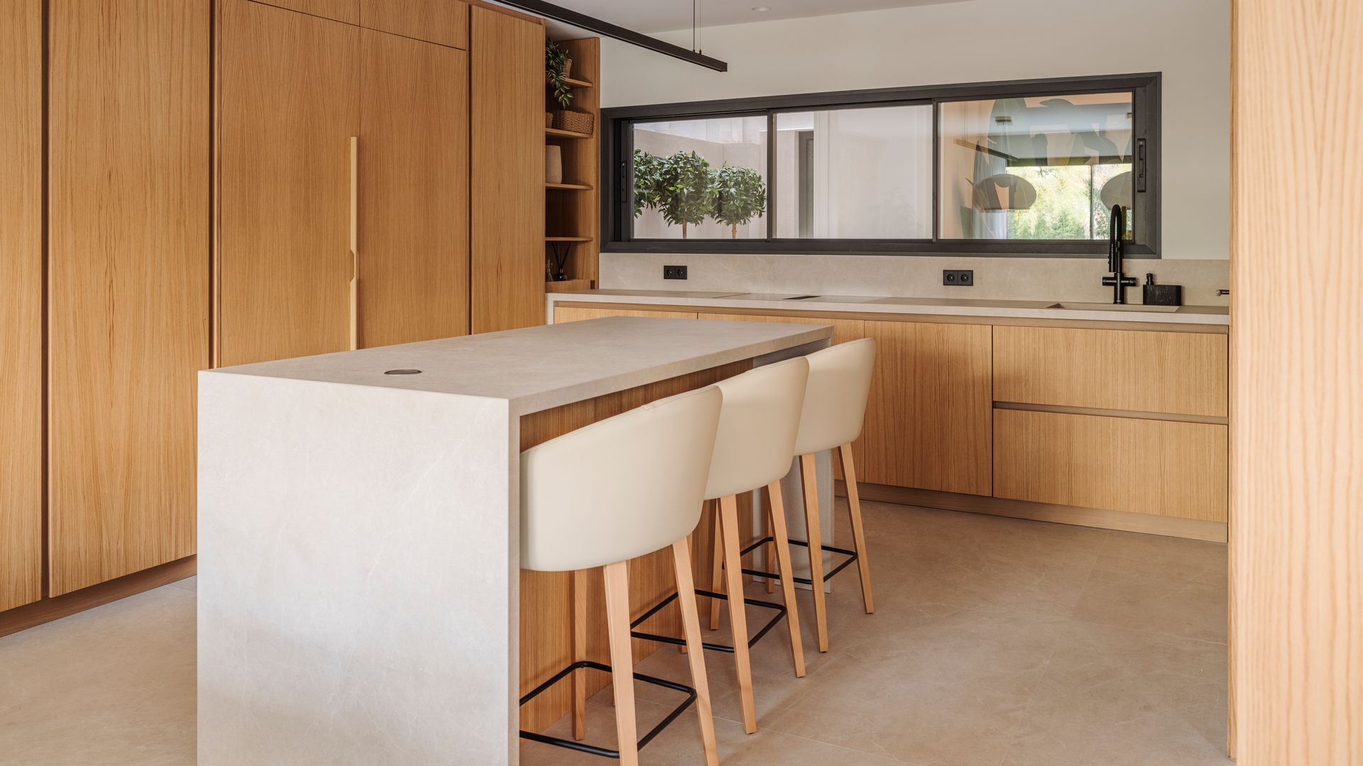 Cocina de madera con isla con taburetes altos, armarios hasta el techo y ventana rectangular 