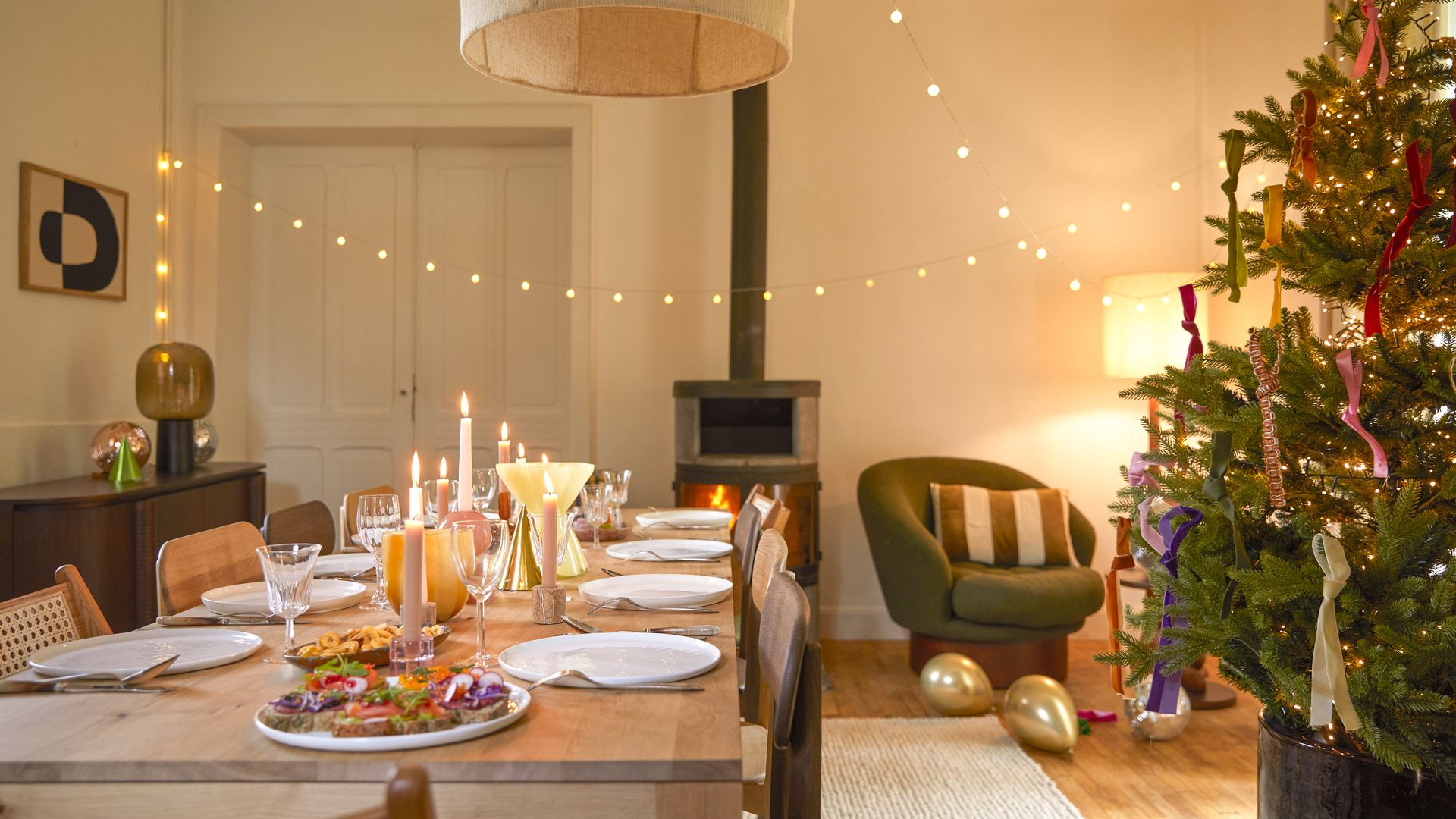 Comedor con chimenea, árbol de Navidad, mesa de madera, mesa de Navidad, guirnalda de luces, lámpara de techo, butaca verde, aparador de madera, alfombra