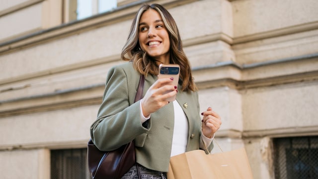 Mujer joven con bolsas de compras y teléfono móvil en la mano