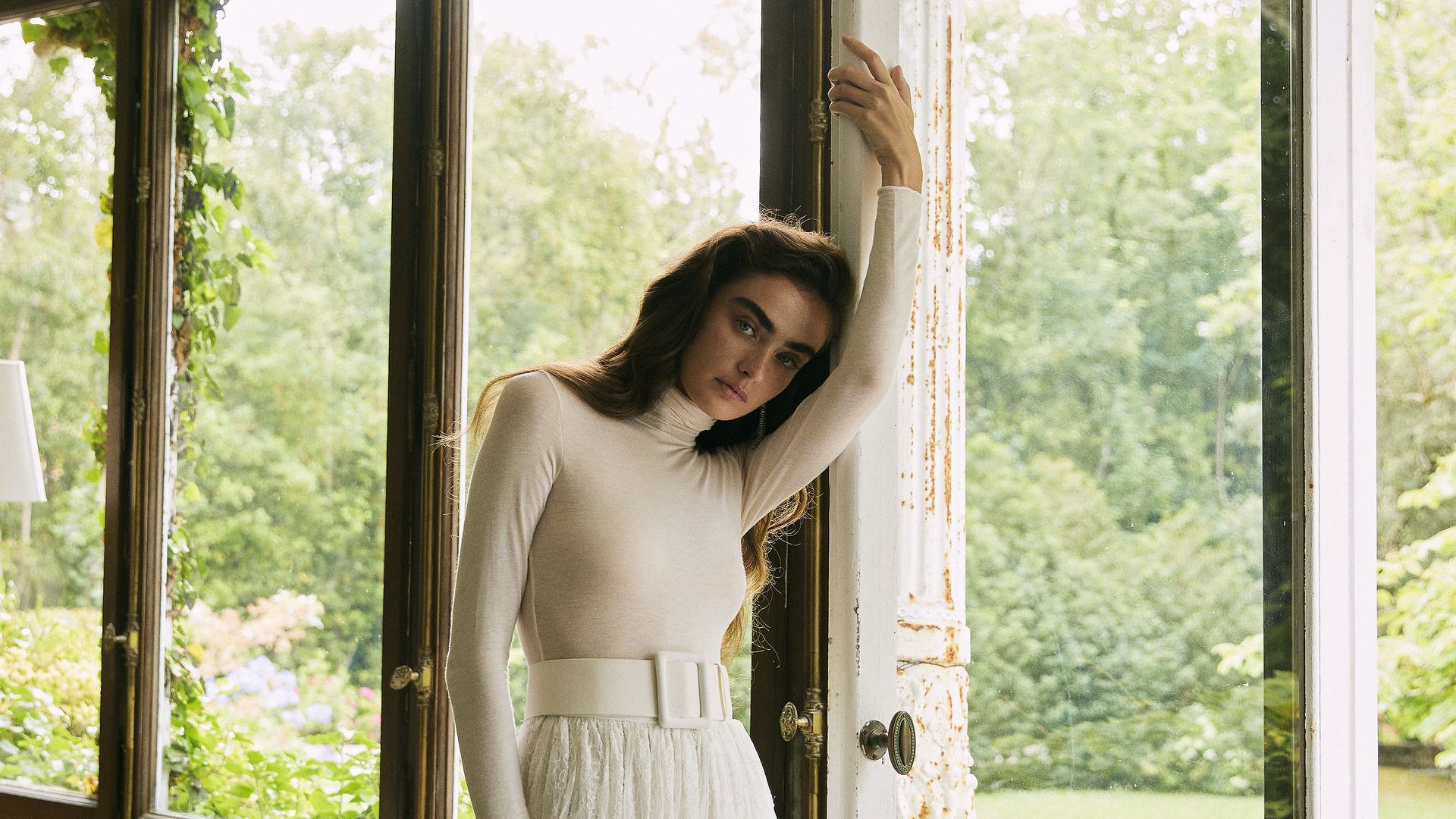 Mujer en un vestido blanco, posando en una sala con ventanas grandes