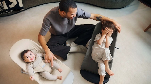 Padre con dos bebés con hamacas de Babybjorn en el salón