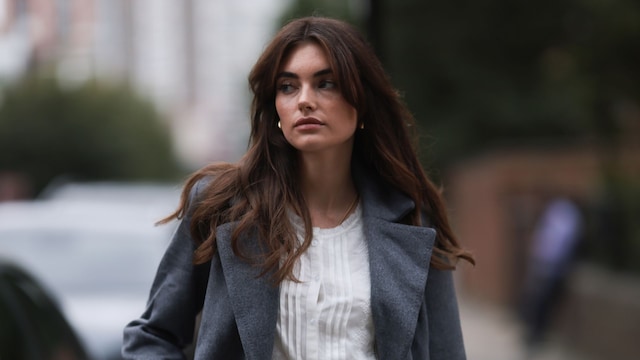 Celine Bethmann con falda corta negra, camisa blanca y abrigo gris en Londres