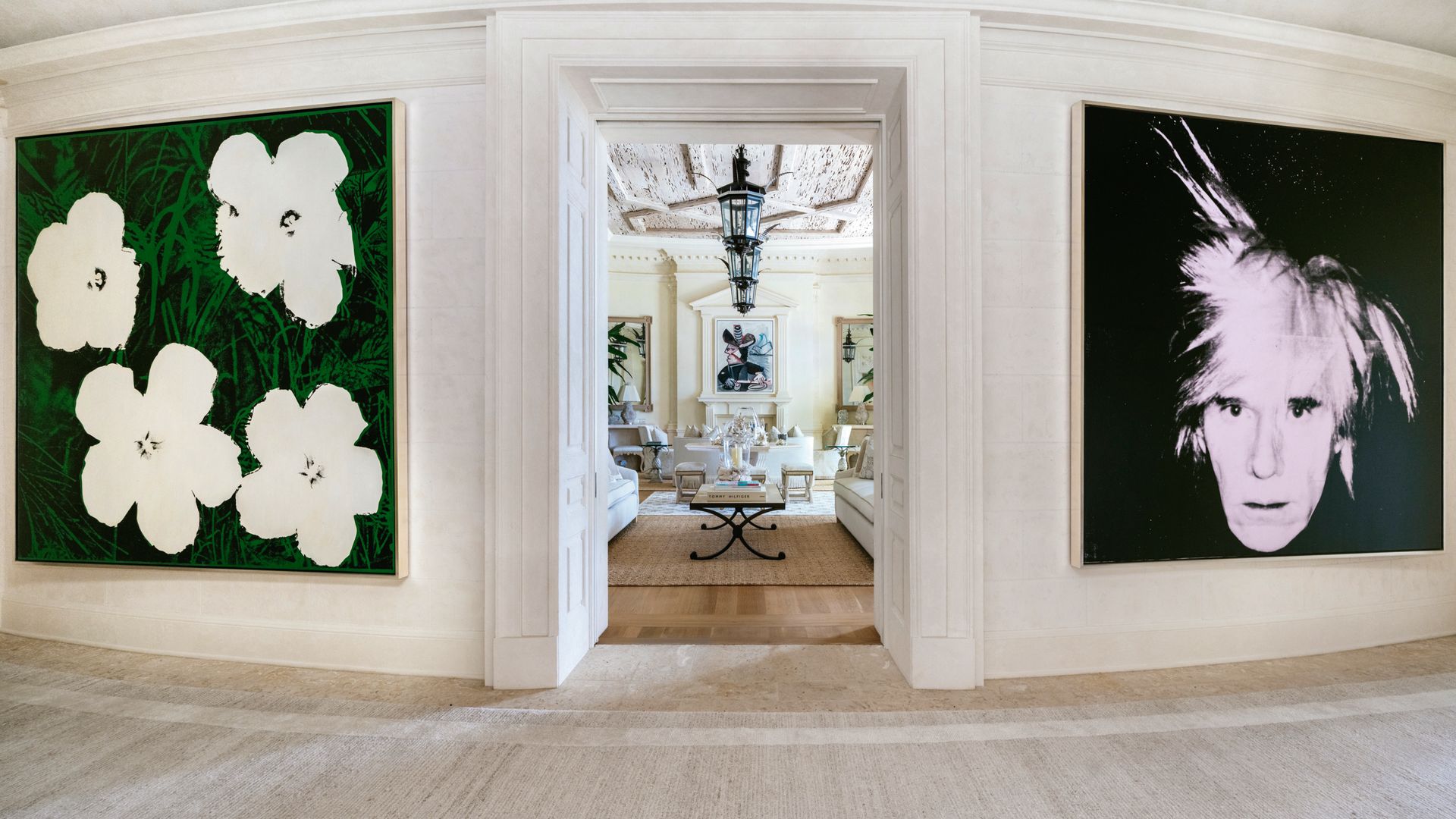 Pared blanca con dos cuadros de Warhols, un autorretrato del artista y "Flowers", de rosas blancas a cada lado de la entrada a una habitación