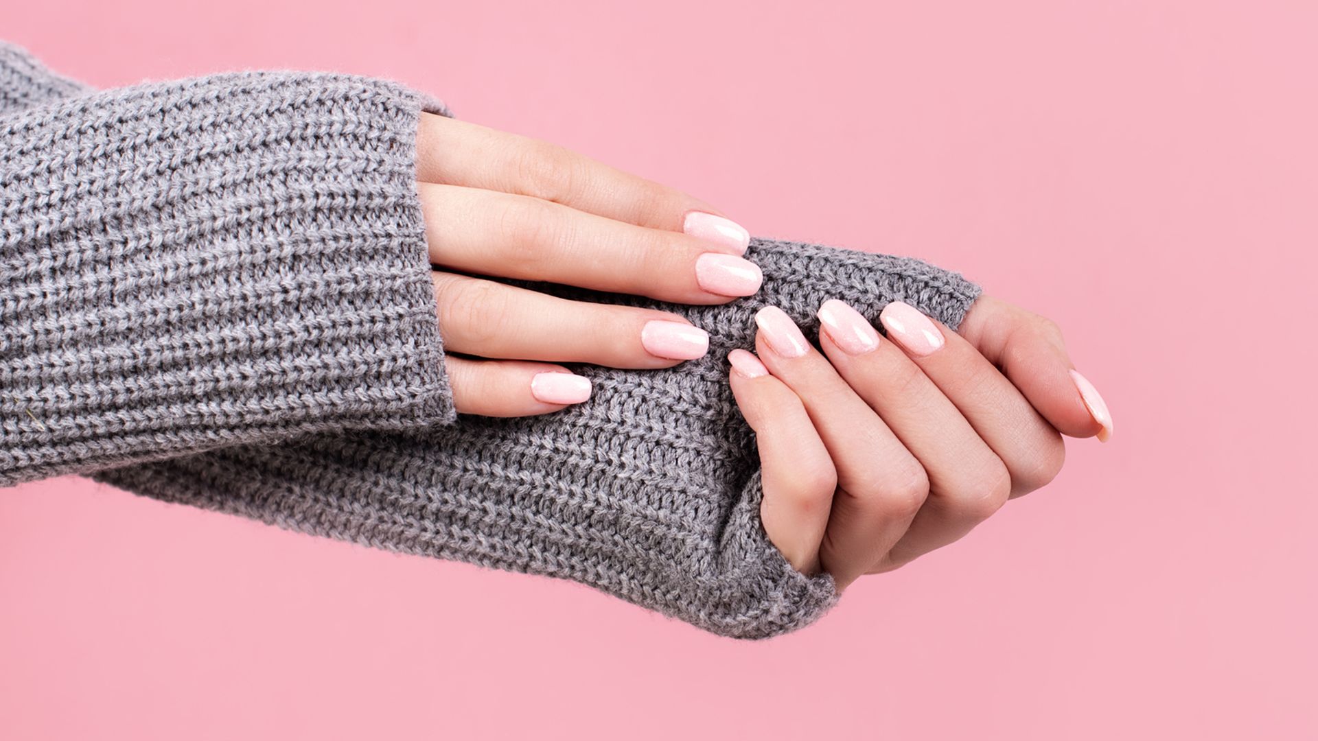 Manos de mujer con manicura rosa y mangas de jersey de punto gris