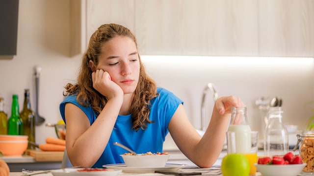 Adolescente angustiada, triste y alterada sentada a la mesa de la cocina. Trastornos alimentarios. Pérdida de apetito. Problemas propios de la adolescencia.