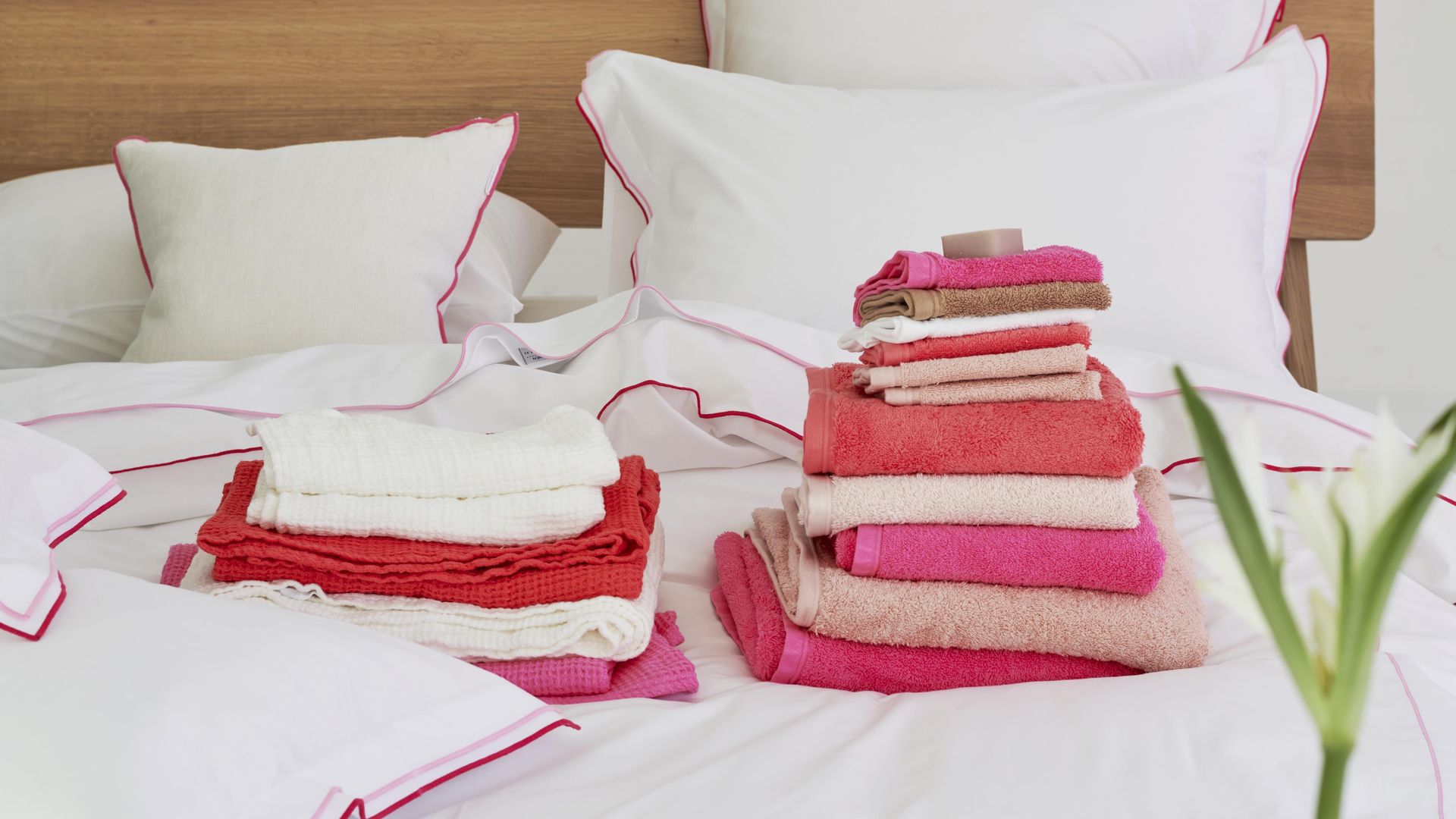 Cama con ropa de cama blanca y una montaña de toallas en rosa, blanco y rojo