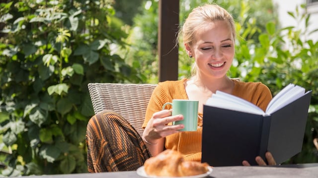 Mujer guapa sosteniendo una taza y leyendo un libro