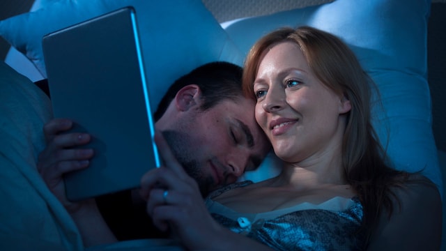 Una mujer leyendo en la cama con su marido
