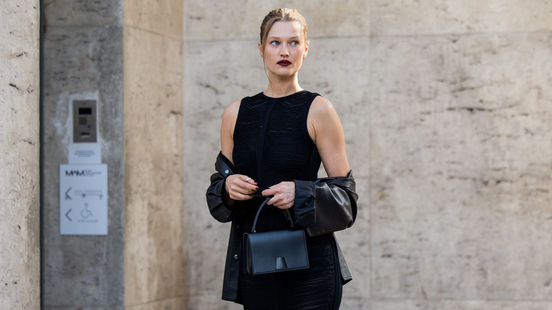 Toni Garrn con vestido negro entallado, cazadora de cuero y bolso negro de mano en Paris