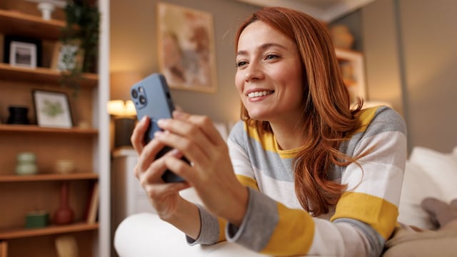 Mujer joven pelirroja sonriente mirando su teléfono tumbada en el sofá