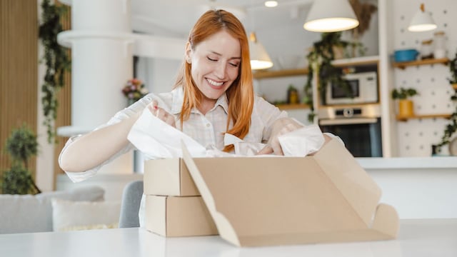 Mujer pelirroja sonriente abriendo una caja en su casa