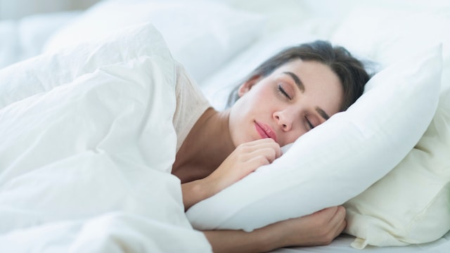 Mujer durmiendo plácidamente en una cama blanca con edredón nórdico que le tapa hasta los hombros