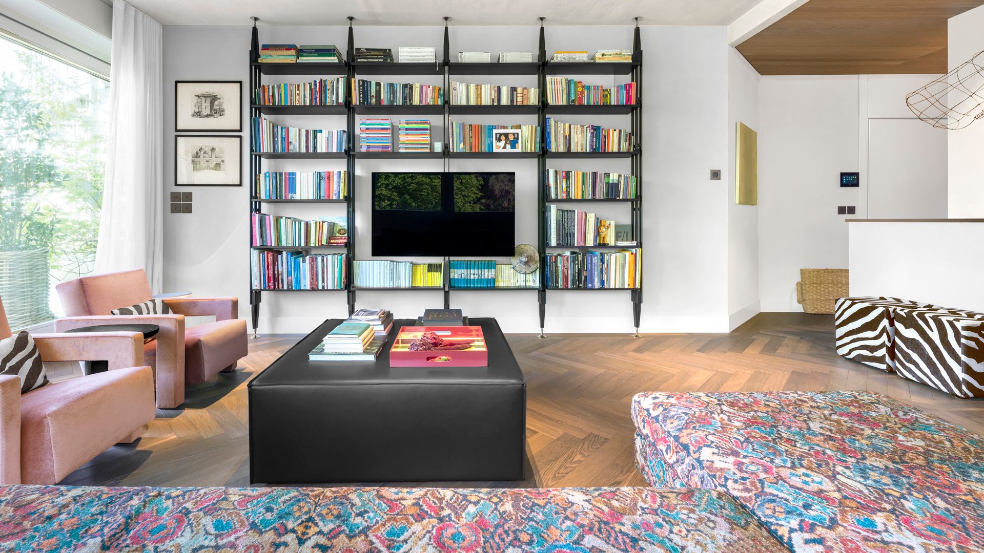 Salón con televisión, estantería negra con libros, sillones rosas, puf de cebra, mesa de centro negra, sofá multicolor