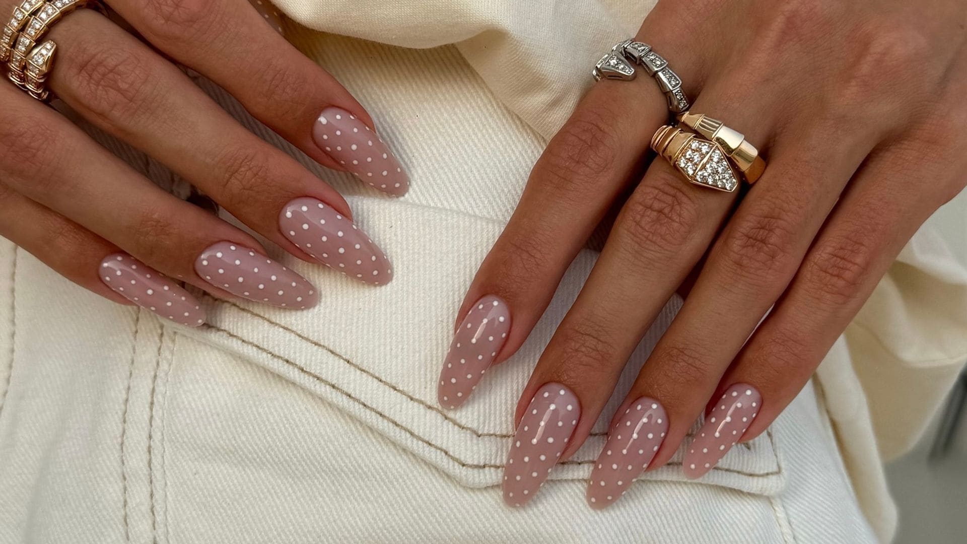 Manos de mujer con anillos de serpientes y uñas largas con manicura de lunares