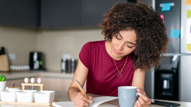 mujer escribiendo en un diario mientras toma una taza de café