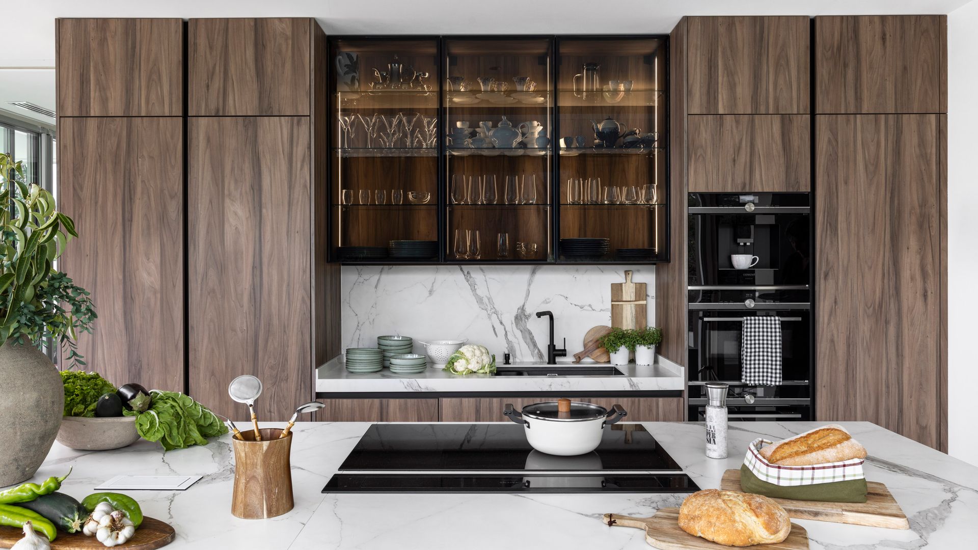 Cocina con isla con encimera de mármol, muebles hasta el techo de madera oscura, vitrina central negra con cristales ahumados