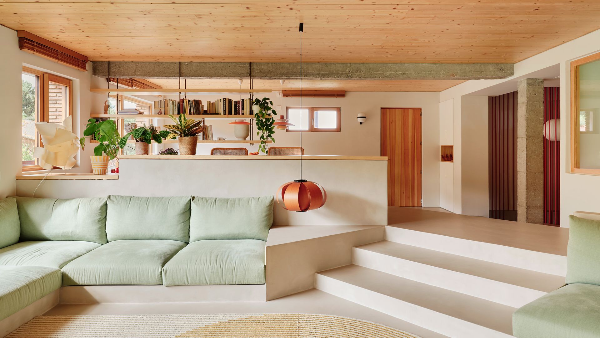 Salón en dos alturas con sofá de obra verde claro, lámpara naranja, techo de madera, alfombra redonda 
