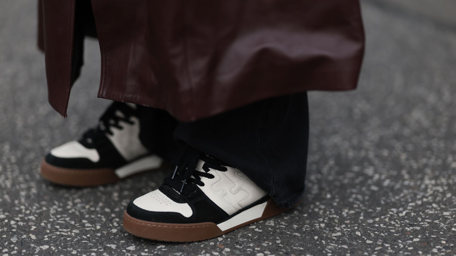 Zapatillas deportivas en blanco y negro en detalle, con pantalones negro y gabardina de cuero burdeos.