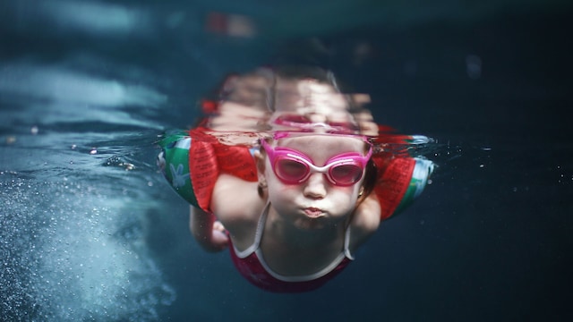 Niña de cuatro años nadando y buceando en la piscina