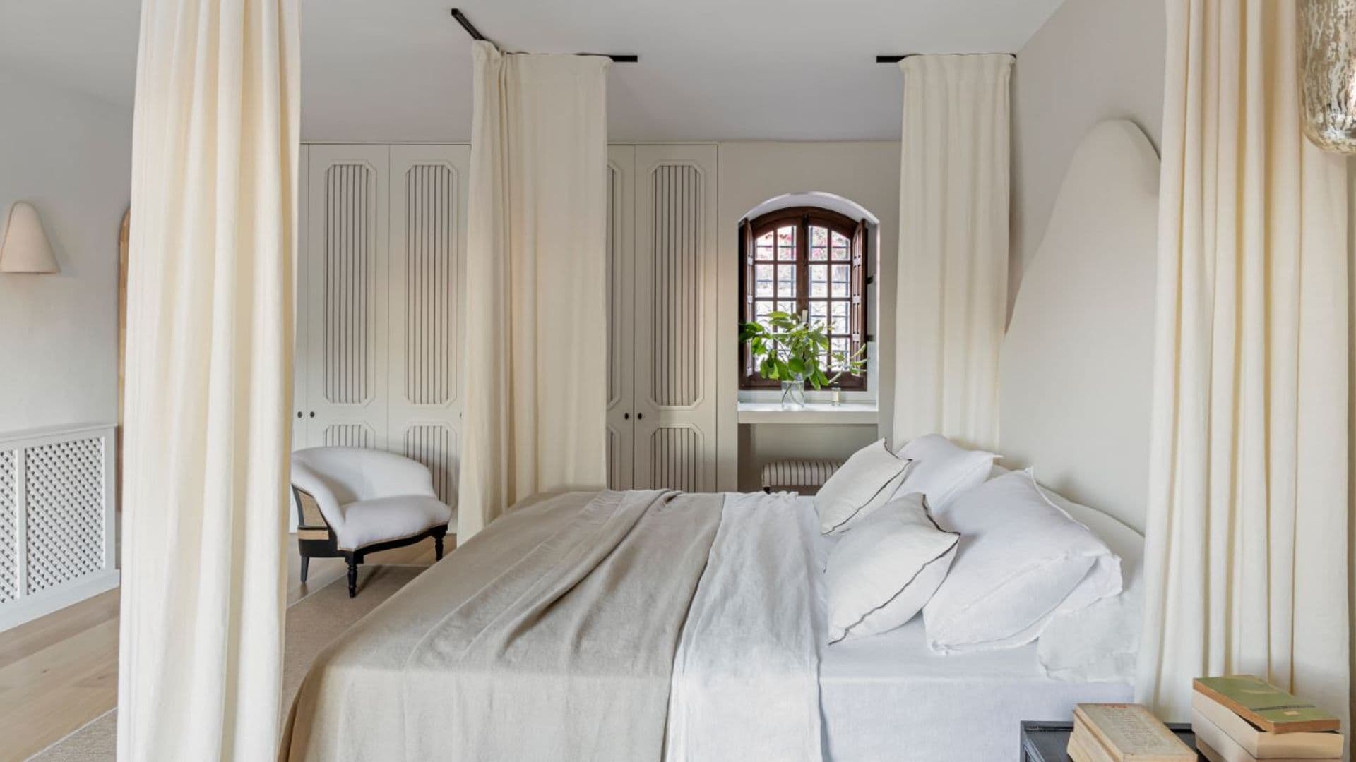 Dormitorio con cortinas tipo dosel, armario con puertas de rejilla, ropa de cama blanca, ventana de madera, planta en el alféizar 