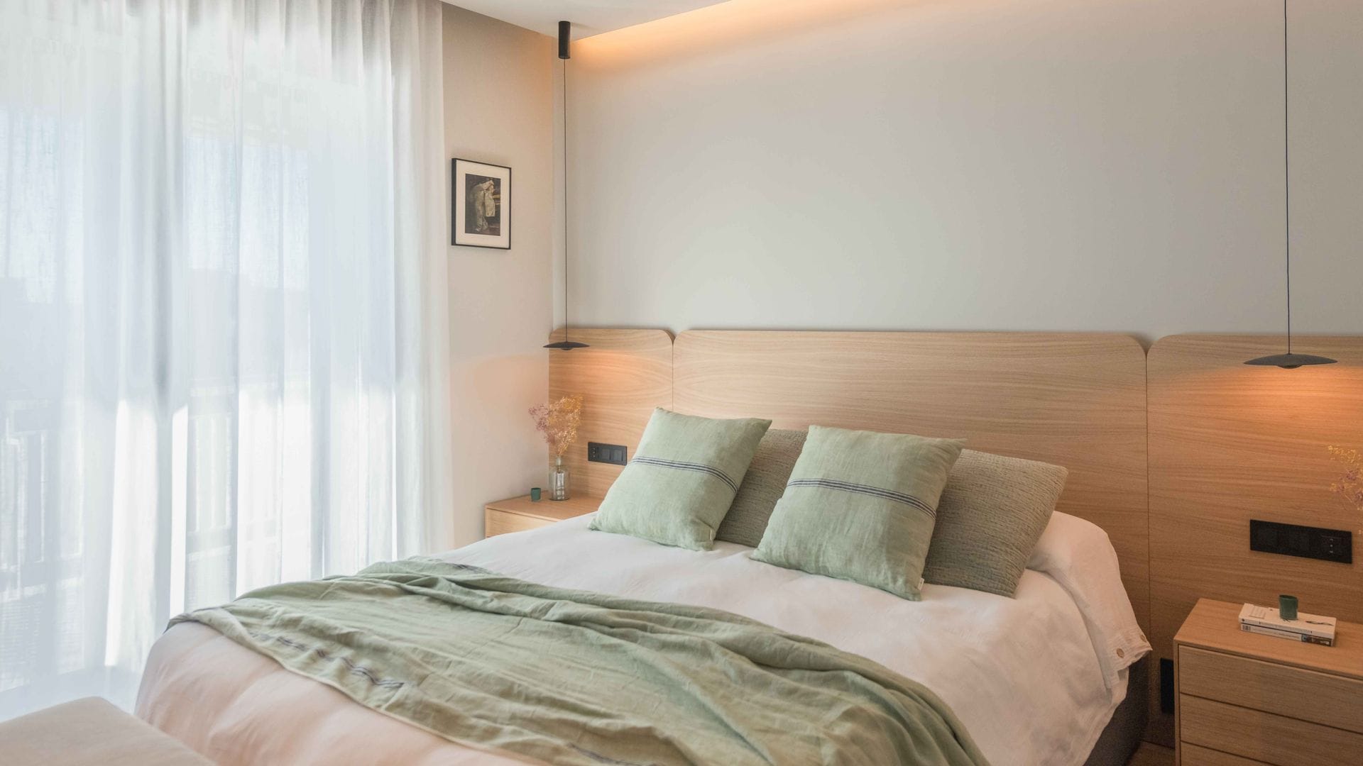 Dormitorio de estilo nórdico con cabecero de madera, lámparas de techo a los lados, ropa de cama verde, sábanas blancas, cortinas blancas