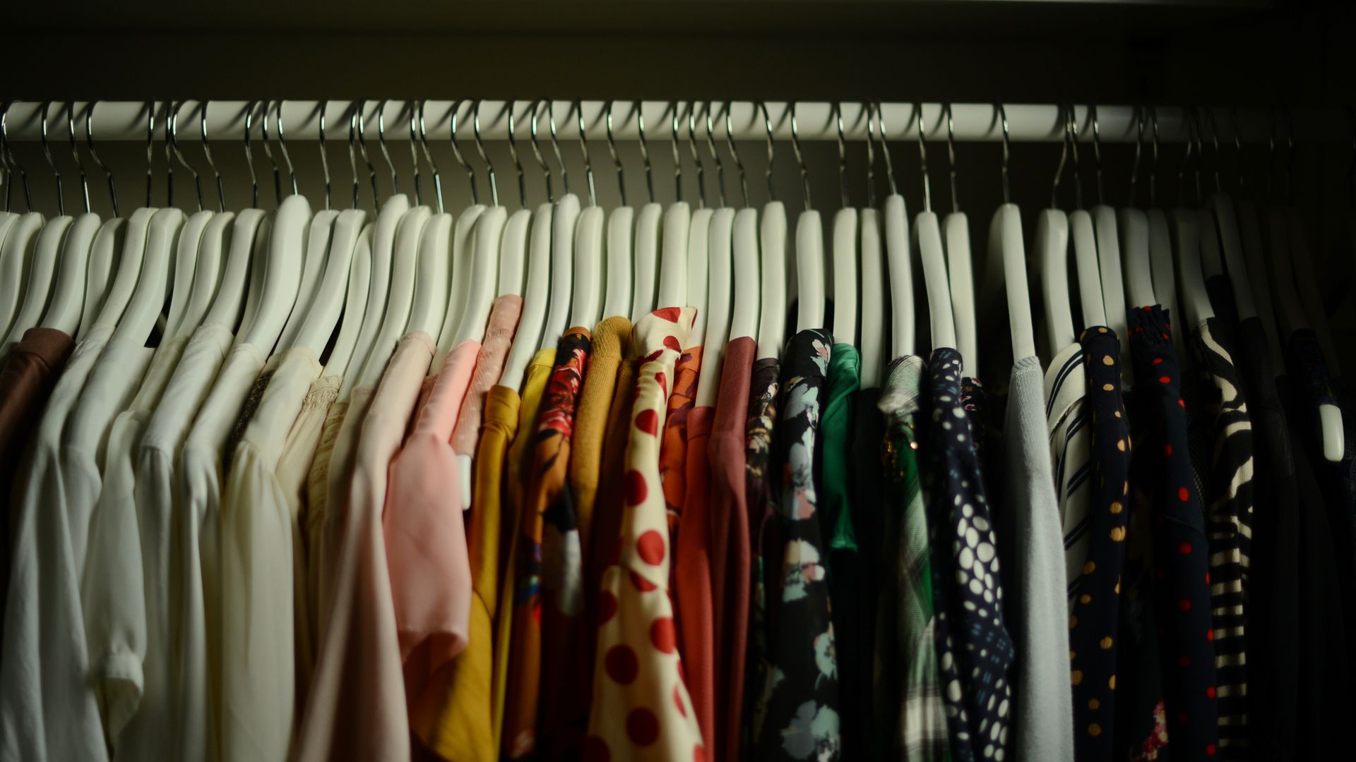 Ropa de muchos colores colgada en el armario en perchas blancas.